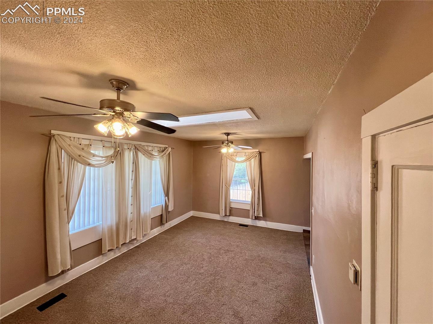 Carpeted empty room with ceiling fan and a textured ceiling