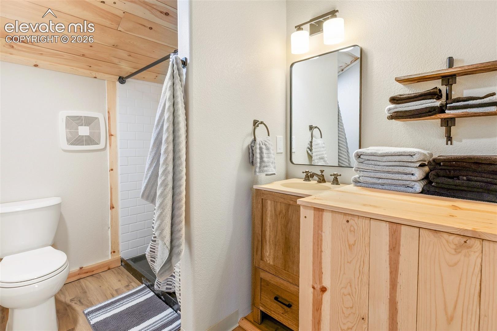 Bathroom featuring wood-plank ceiling, natural wood-finish cabinetry, built-in open shelving, rectangular wall-mounted mirror, and subway-tiled shower surround