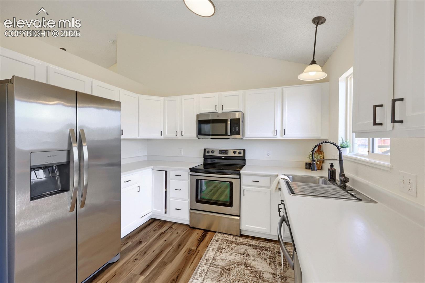 Kitchen featuring white cabinetry, stainless steel appliances, white countertops, wood-finish flooring, and a vaulted ceiling