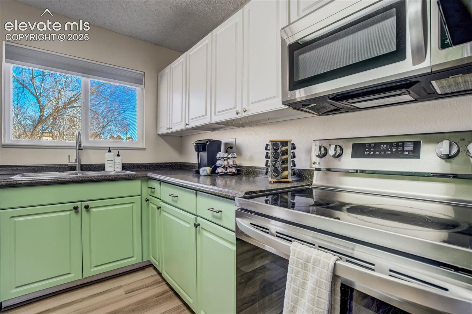 Kitchen featuring a window, wood-finish flooring, stainless steel appliances, upper white cabinetry, and lower green cabinetry