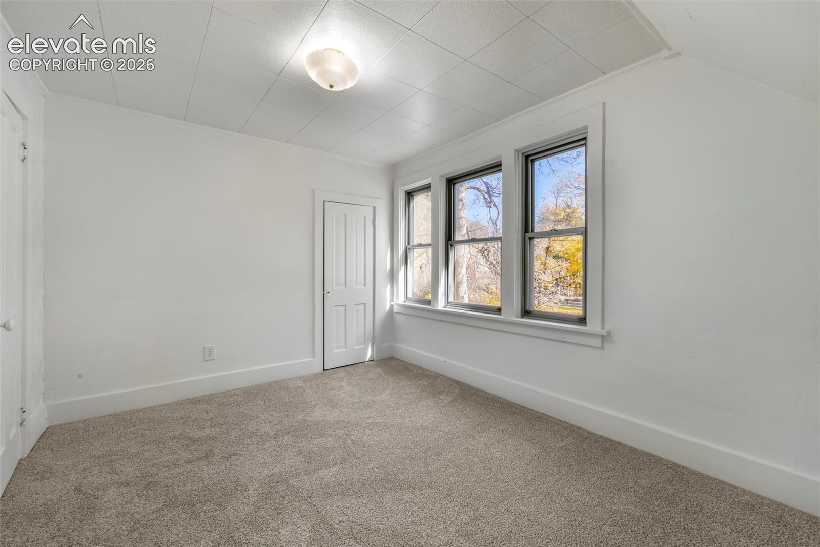 Neutral-toned wall-to-wall carpeting, three-panel interior door, triple-pane window configuration, and recessed flush-mount ceiling fixture
