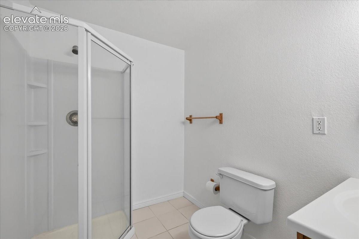 Corner shower enclosure with built-in shelving, tile flooring, and a wall-mounted towel bar
