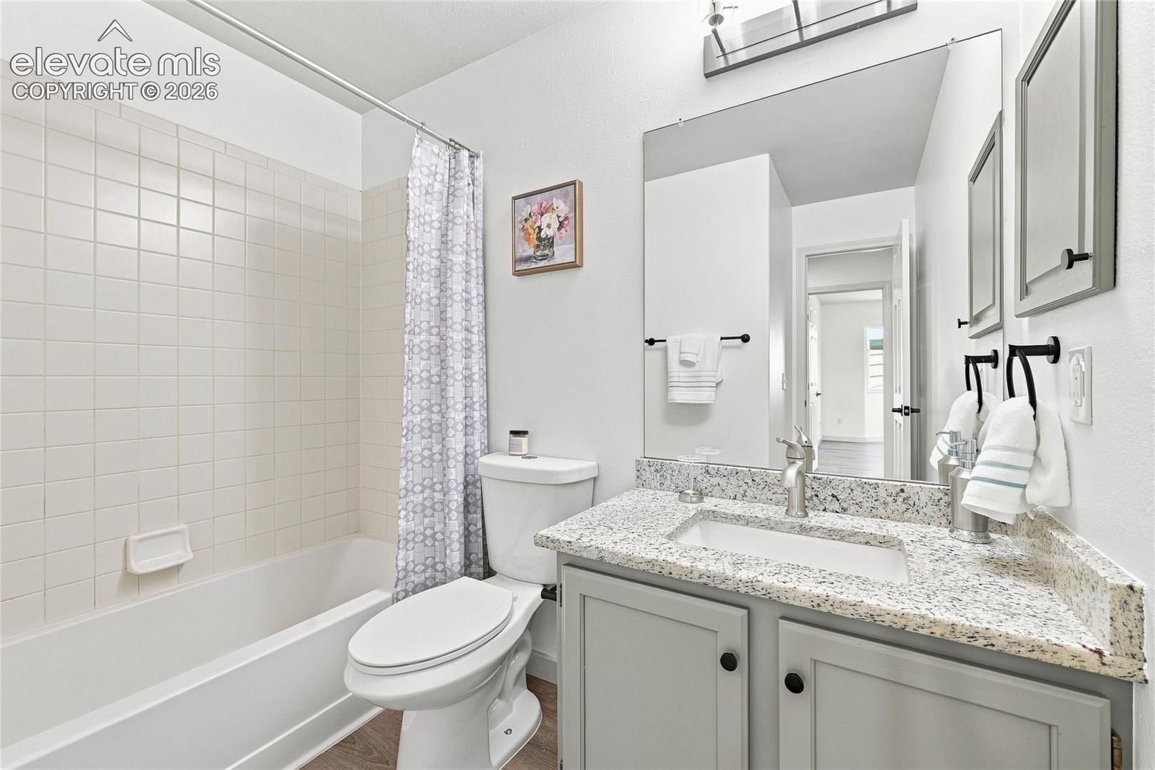 Bathroom featuring a tub/shower combination with white tile surround, a vanity with a light-toned countertop, and a large wall-mounted mirror