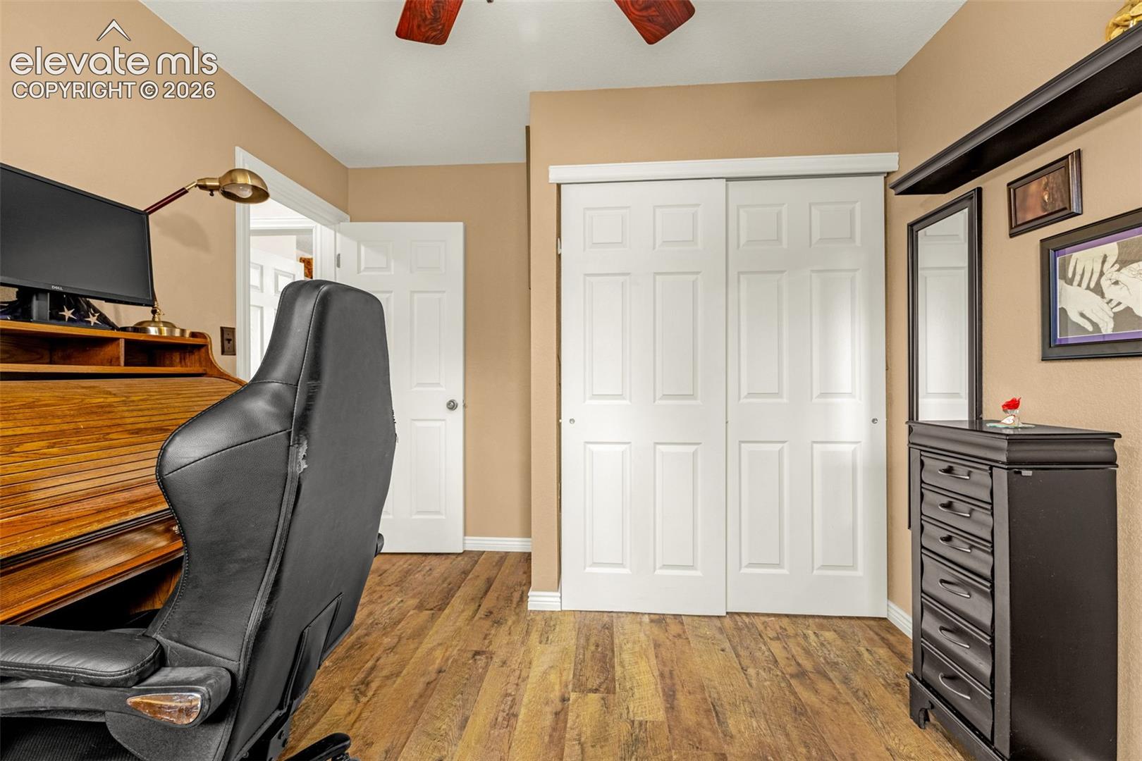 Wood-finish flooring, white six-panel interior door, and white six-panel sliding closet doors with overhead shelving