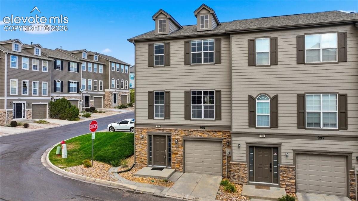 Multi-story end unit townhome featuring stone and siding exterior, multiple windows with decorative shutters, integrated garage, and a dormer window