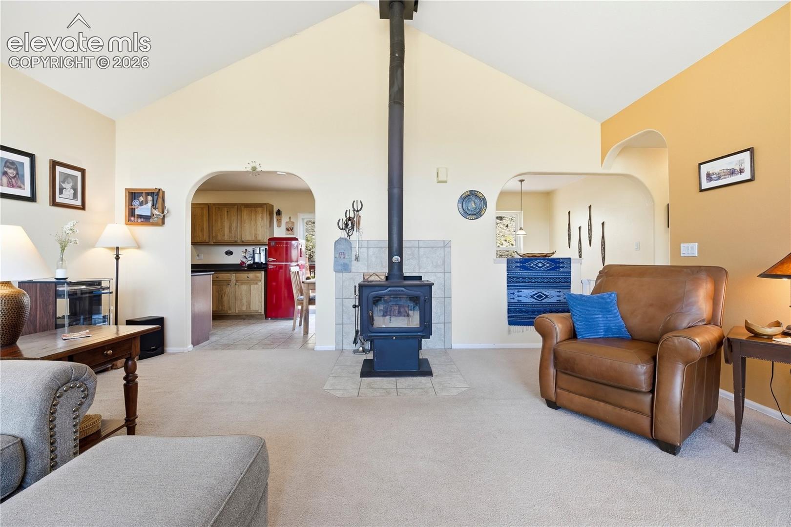 Vaulted ceiling, wood-burning stove with a tiled hearth, arched doorways, and light-toned carpeting