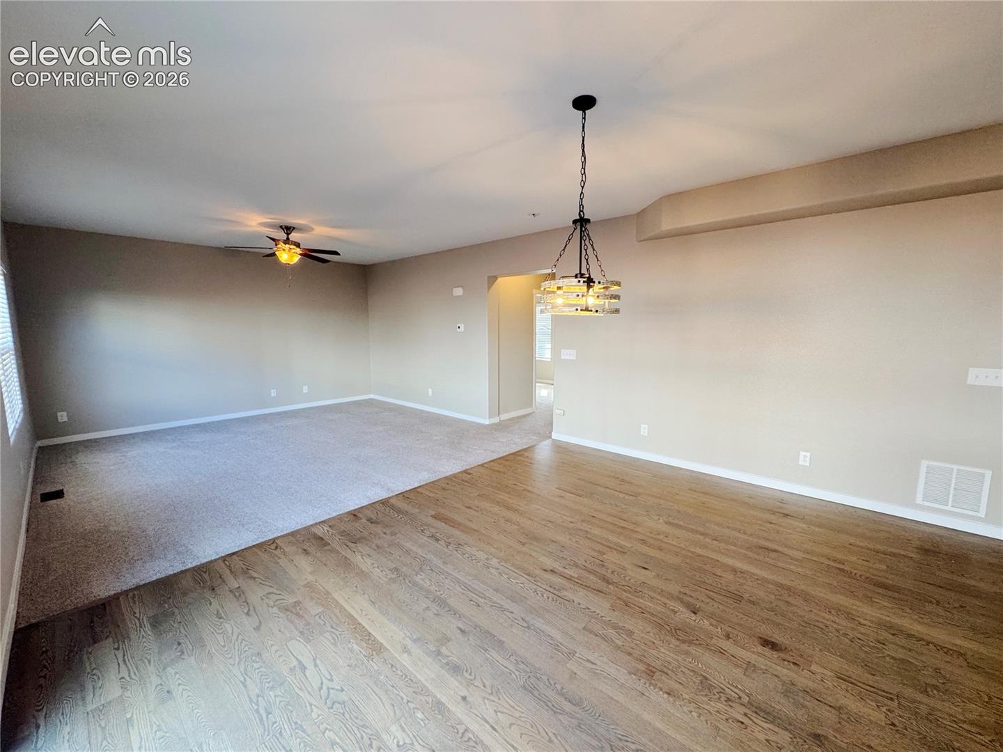 Open-concept space featuring wood-finish flooring, neutral wall tones, a ceiling-mounted light fixture with multi-tiered glass shades, and a dual-blade ceiling fan