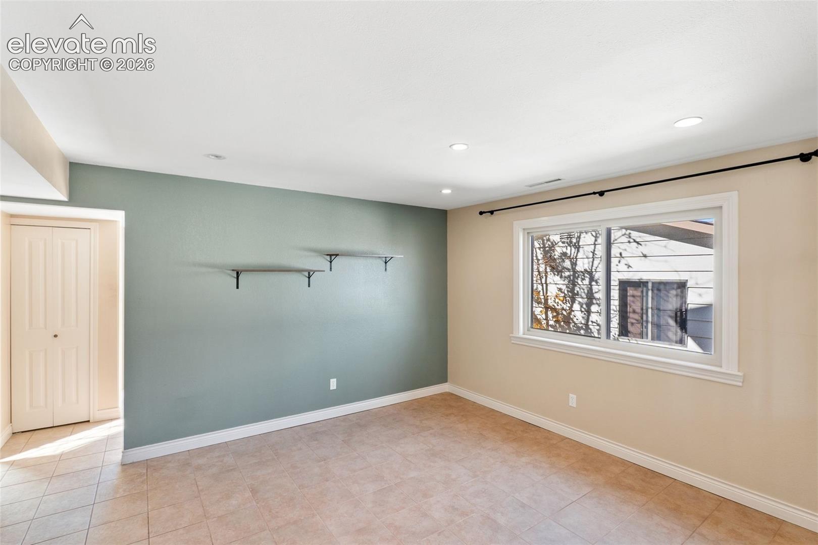 Room featuring tile flooring, a dual-tone wall finish with a green accent wall, wall-mounted shelving, recessed lighting, and a window with an integrated curtain rod