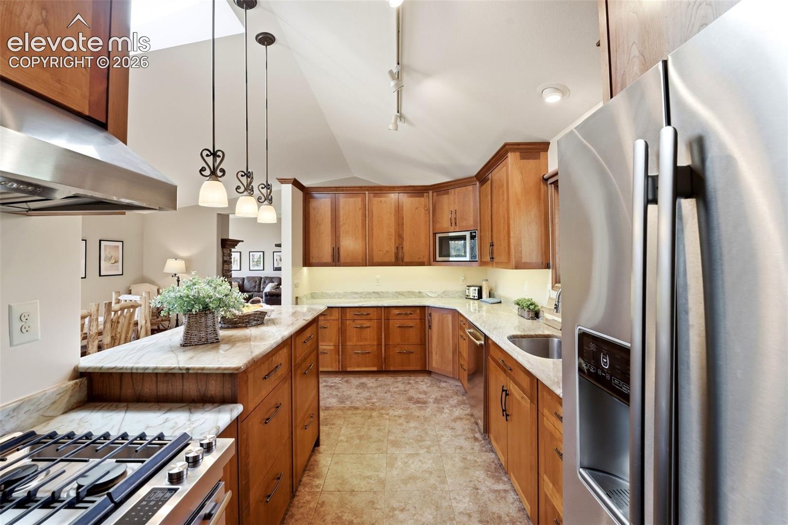 Kitchen featuring wood cabinetry, stainless steel appliances, pendulum lighting, and stone countertops