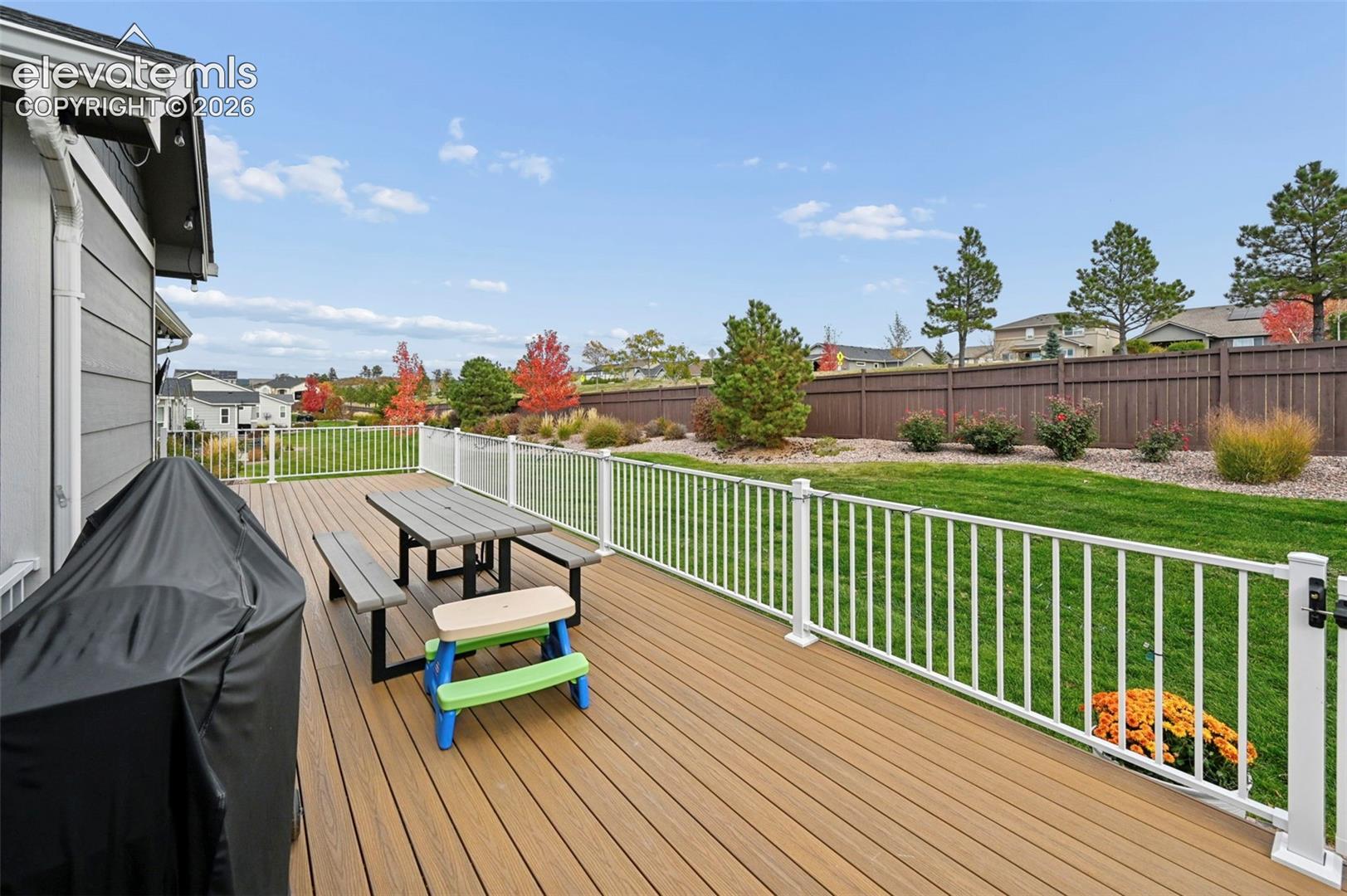 Spacious composite deck featuring a white metal railing and a backyard with mature landscaping