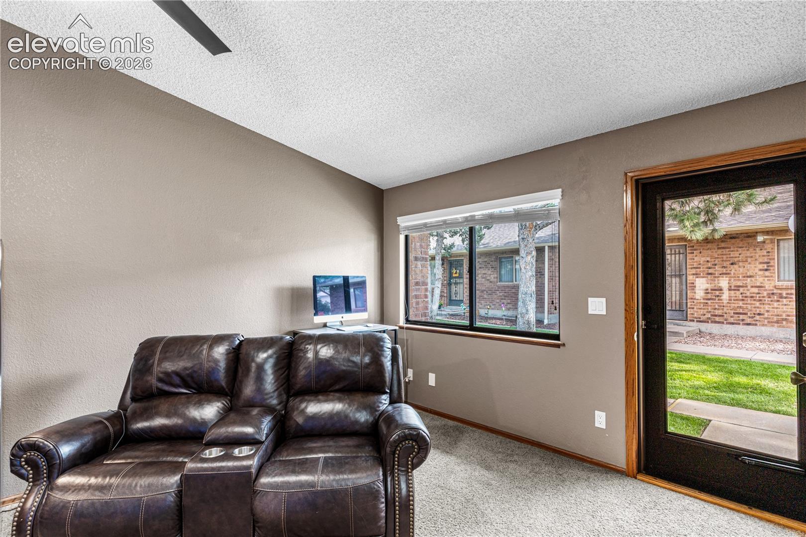 Room featuring a vaulted ceiling with an integrated fan, neutral-toned walls, carpeting, and a glass-paneled exterior door with a wood-finished frame