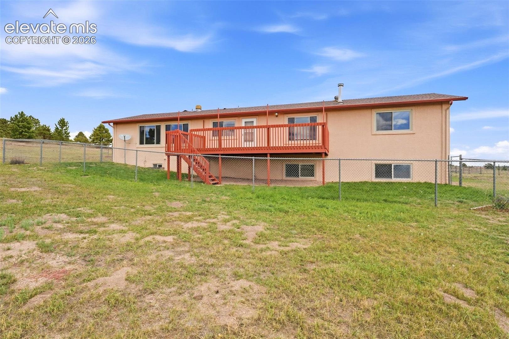 Expansive sloped yard featuring chain link fencing and a stucco exterior with multiple windows