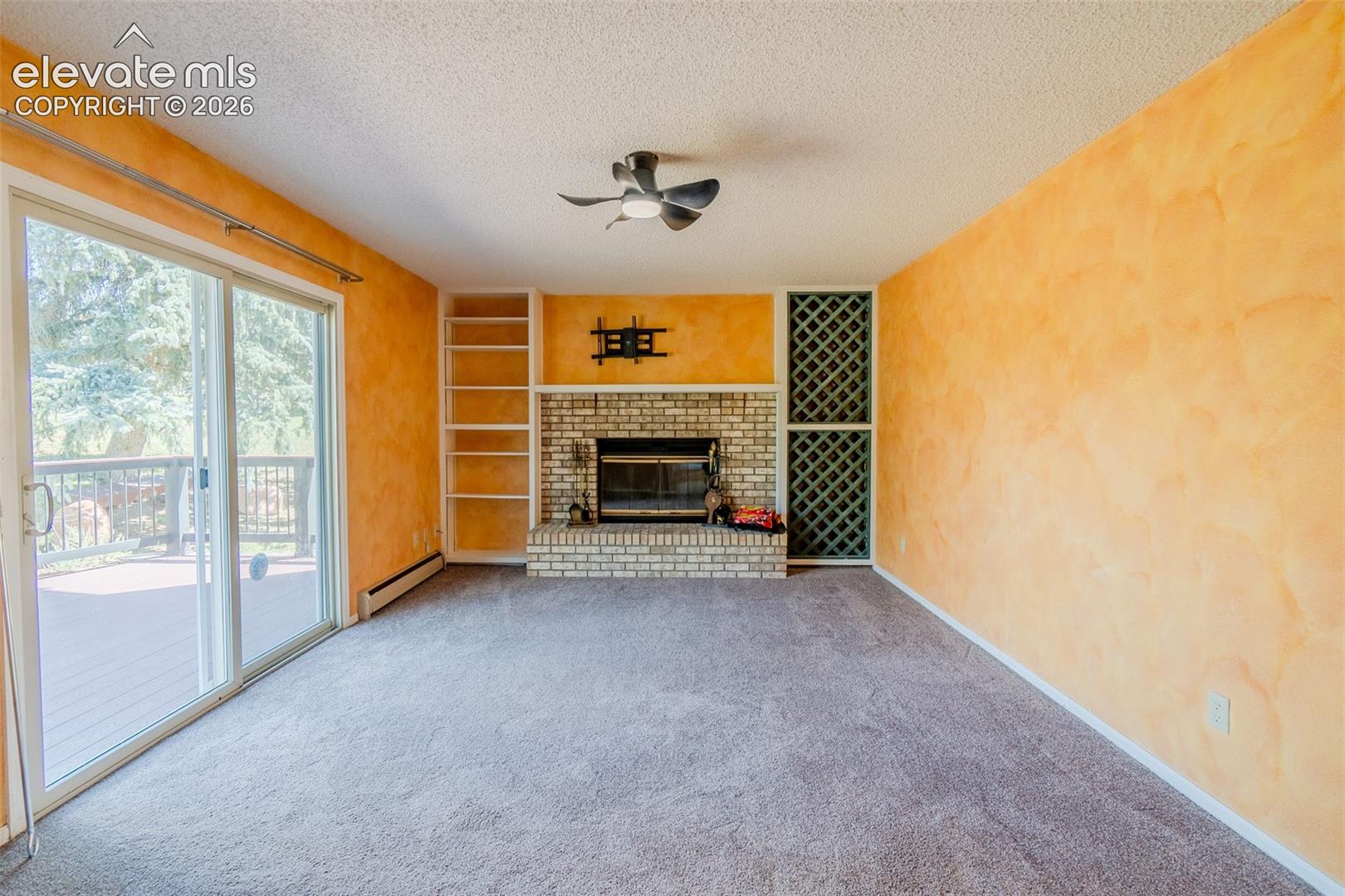 Brick fireplace with hearth, built-in shelving, built-in wine rack, ceiling fan, and sliding glass door