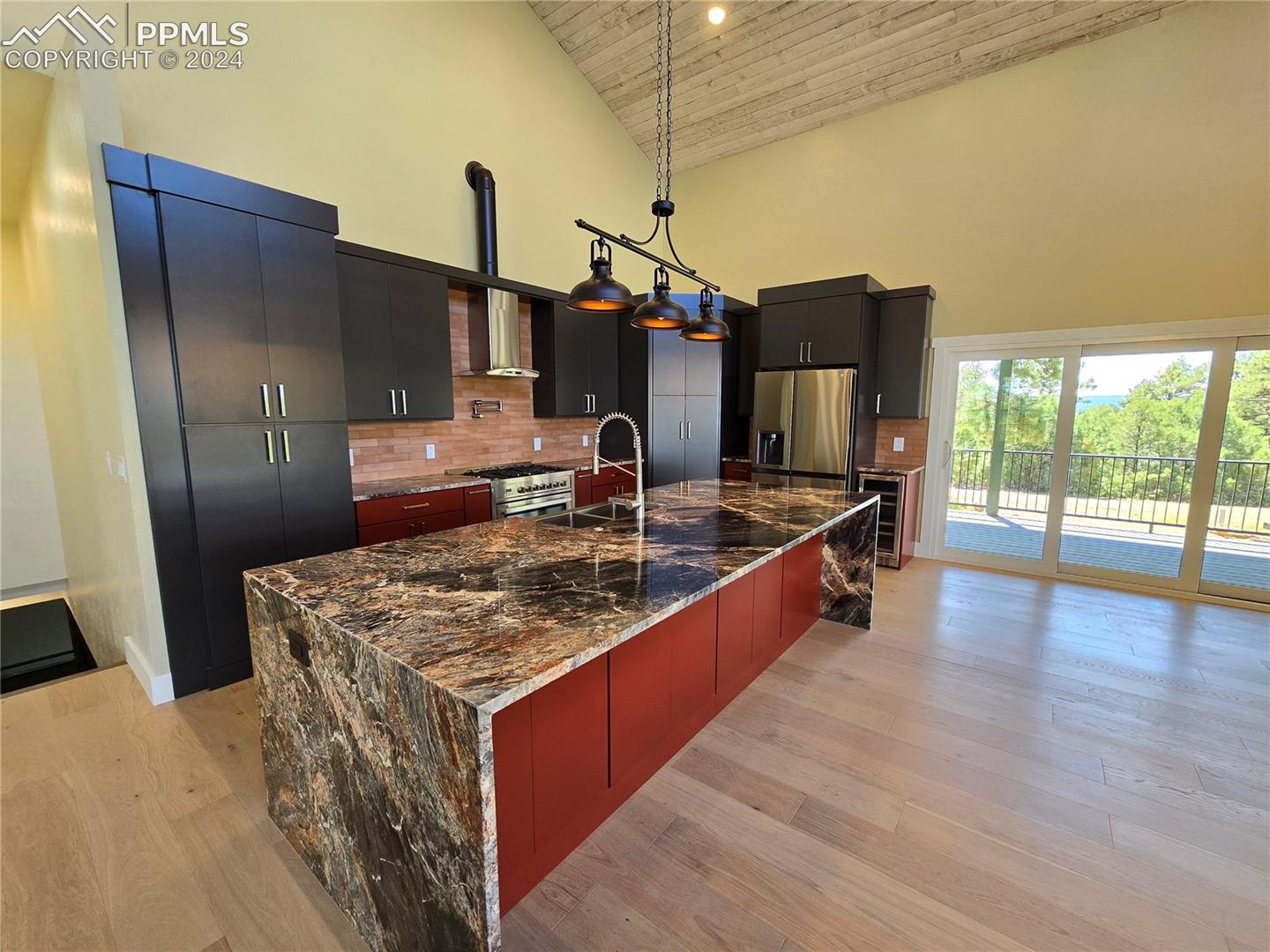 Kitchen featuring hanging light fixtures, appliances with stainless steel finishes, a large island with sink, high vaulted ceiling, and tasteful backsplash