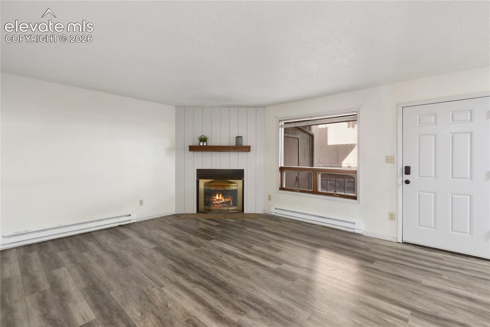 Living area featuring wood-finish flooring, a corner fireplace with a wood mantel, and vertical plank accent wall
