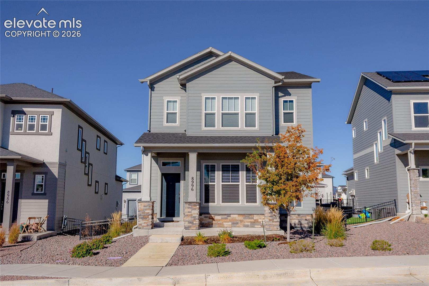 Two-story residence featuring horizontal lap siding, stone veneer accents, multi-pane windows, covered front entryway, and a concrete walkway