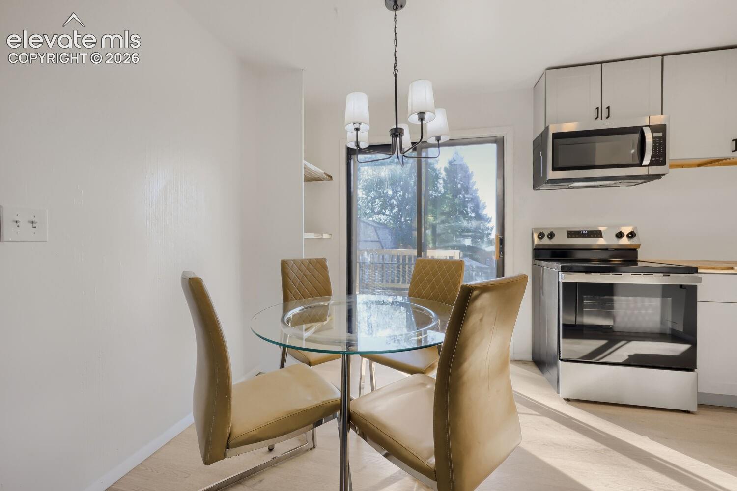 Stainless steel range and microwave, light wood-finish flooring, and white cabinetry with dark hardware