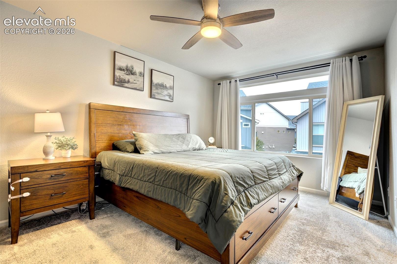 Neutral carpeting, ceiling fan with integrated lighting, and expansive window with horizontal transom