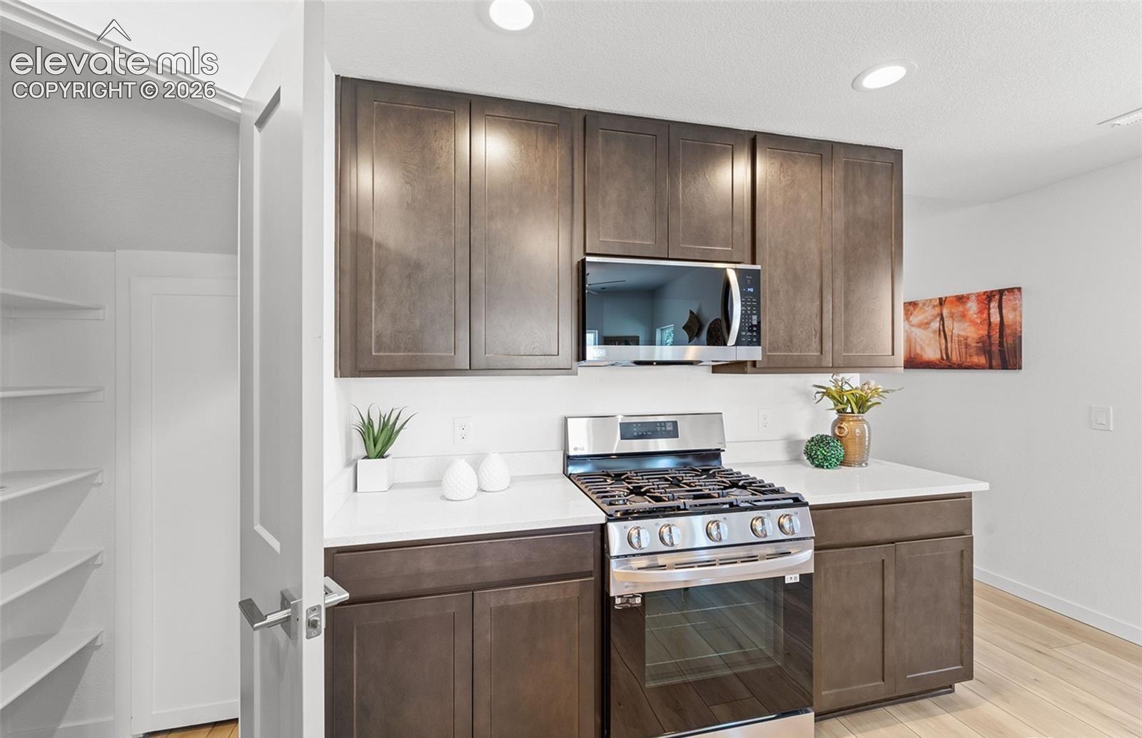 Kitchen featuring dark-toned cabinetry, solid-surface countertops, built-in stainless steel microwave, gas range, and a walk-in pantry with integrated shelving