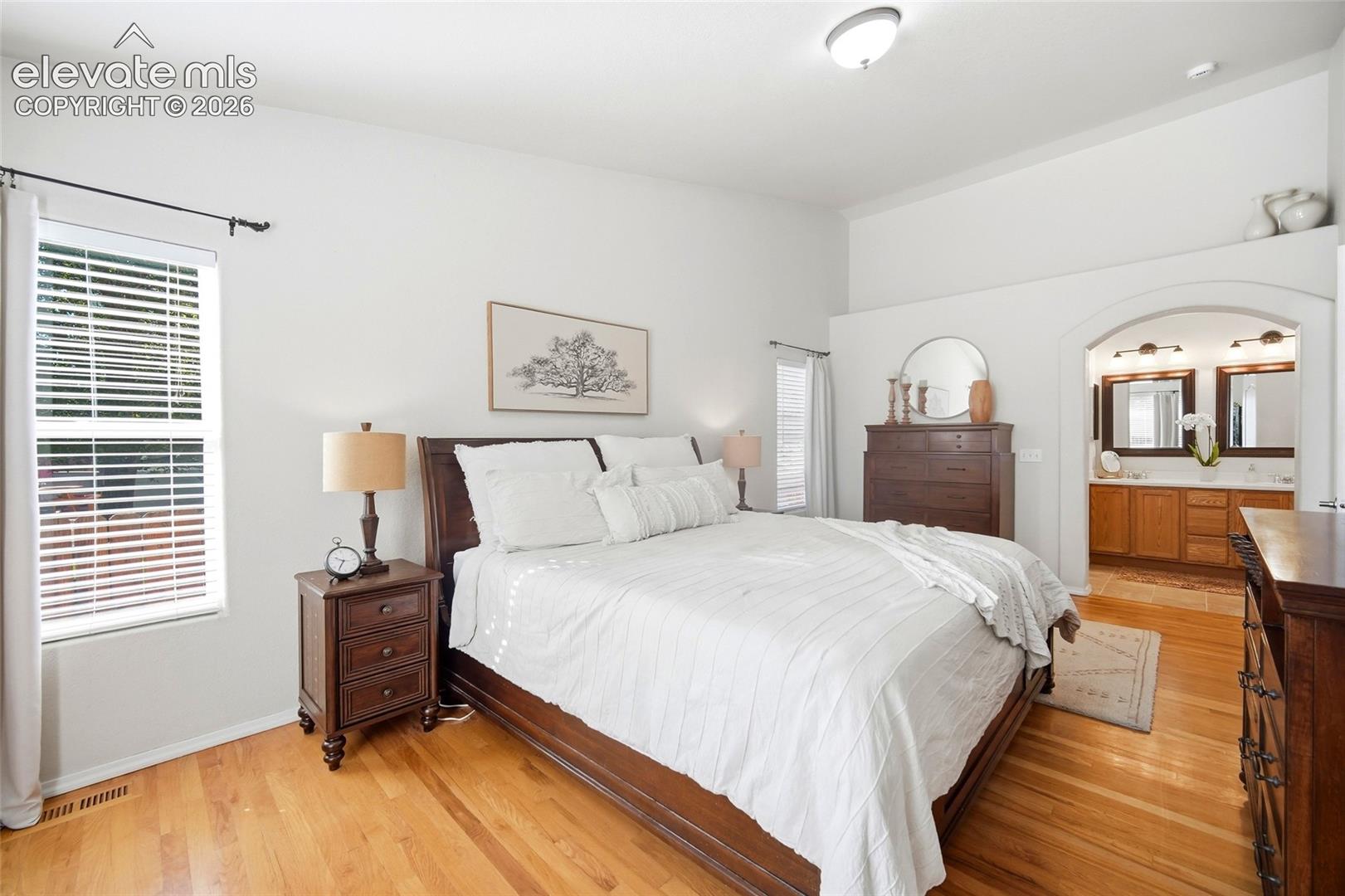 Vaulted ceilings, wood-finish flooring, arched entryway, dual vanity, and built-in medicine cabinets