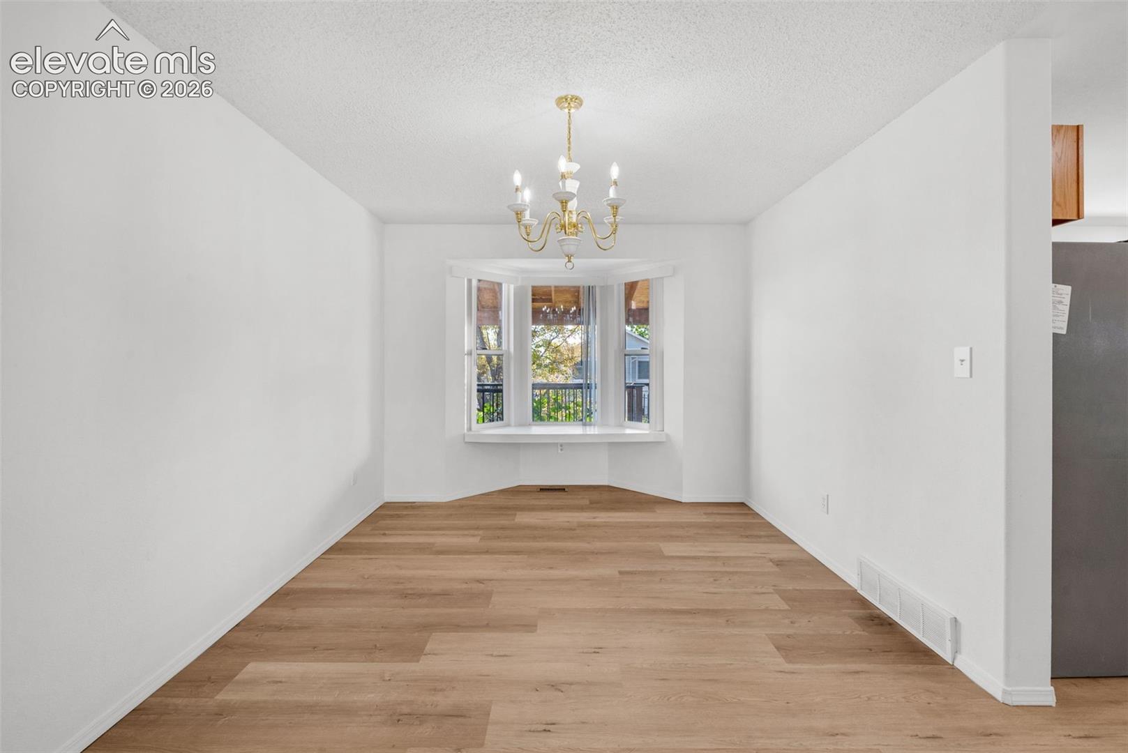 Recessed bay window, brass-finish chandelier, wood-finish flooring, white painted walls