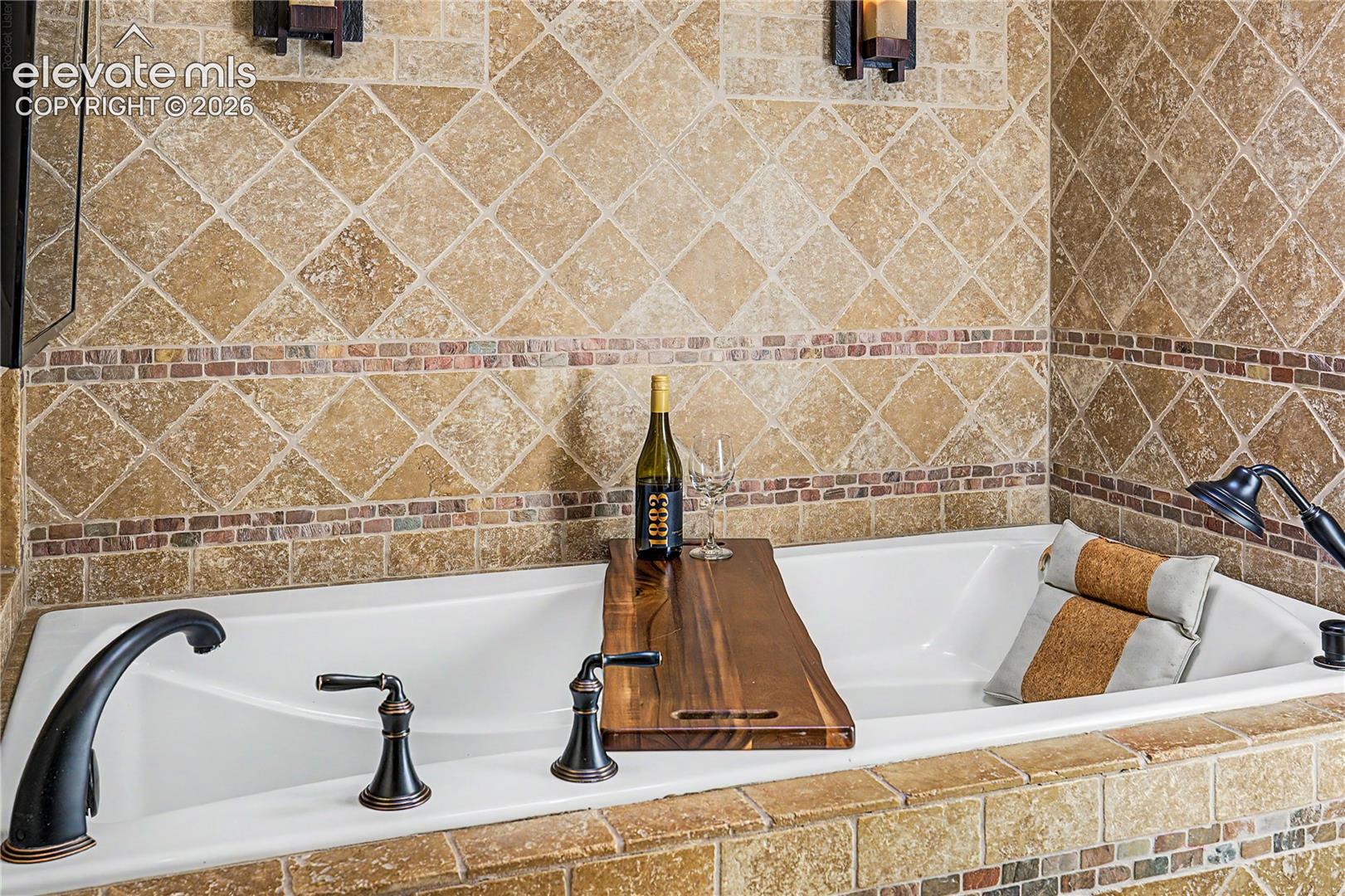 The primary bath's deep soaking tub, wrapped in warm travertine diamond tile, offers a private retreat after a day in the Colorado mountains.