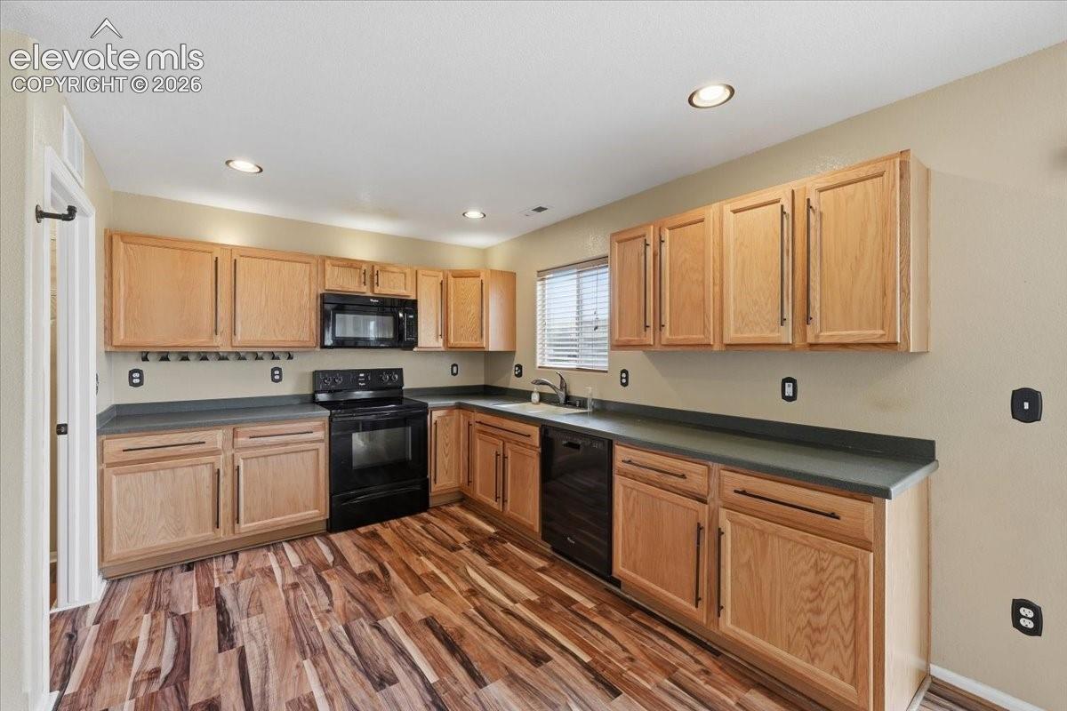Kitchen featuring wood-finish flooring, recessed lighting, wood cabinetry, and dark countertops