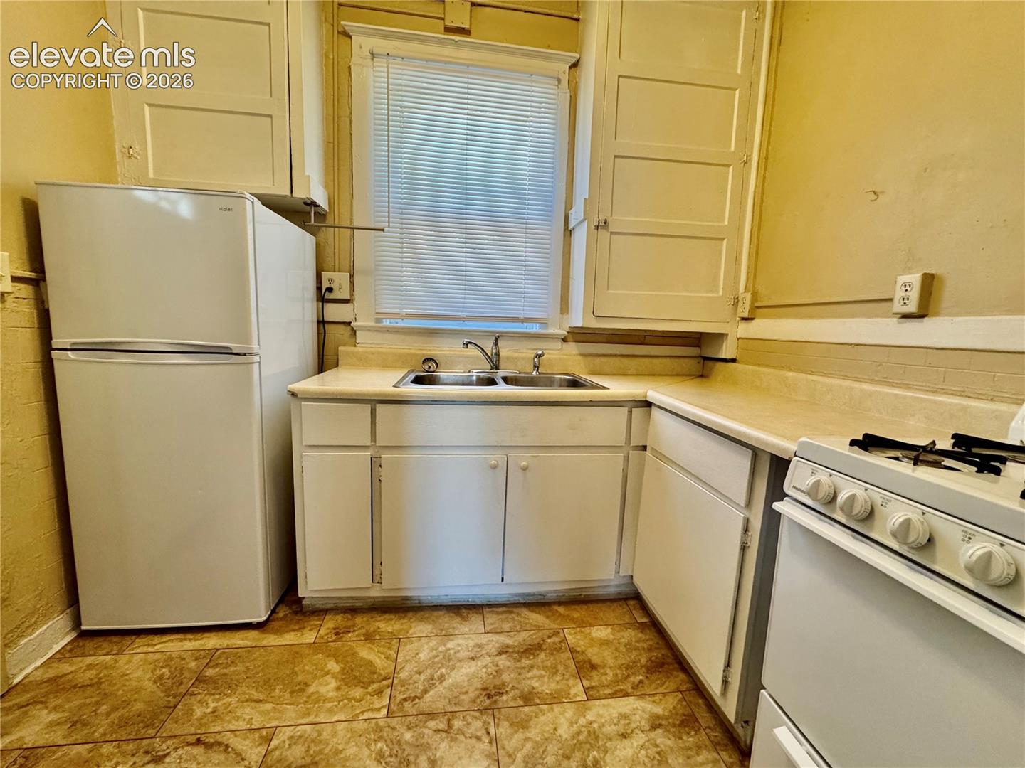 Kitchen featuring a double basin sink, white cabinetry, a window with blinds, and tile flooring