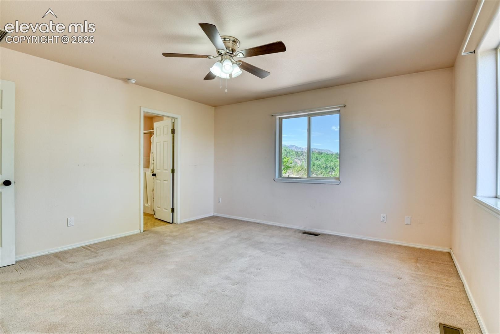 Neutral carpeted flooring, multi-blade ceiling fan with integrated lighting, sliding window with mountain scenery, and six-panel interior door