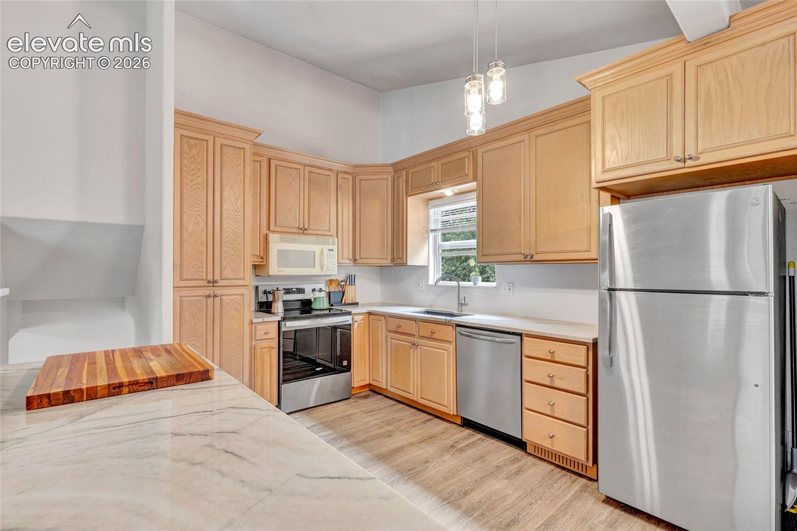 Kitchen featuring light wood cabinetry, stainless steel appliances, a window above the sink, light-toned countertops, and wood-finish flooring