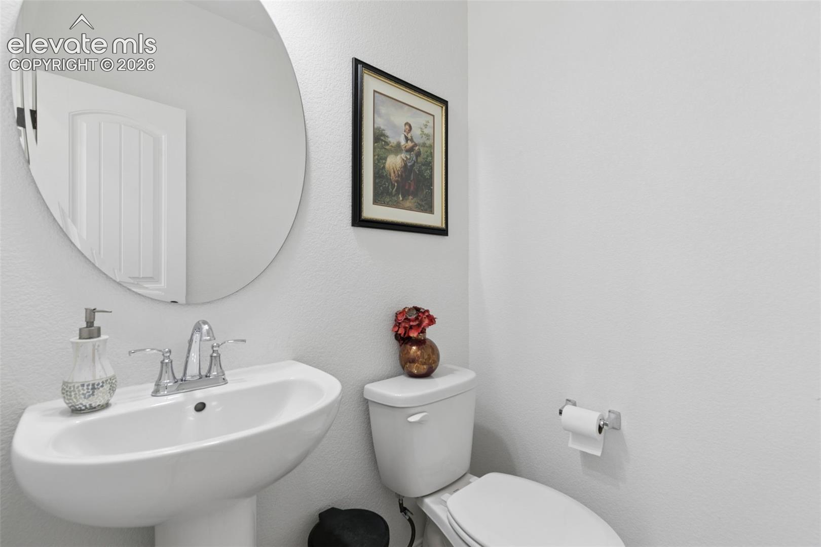 Pedestal sink with chrome faucet, oval wall mirror, and a white toilet