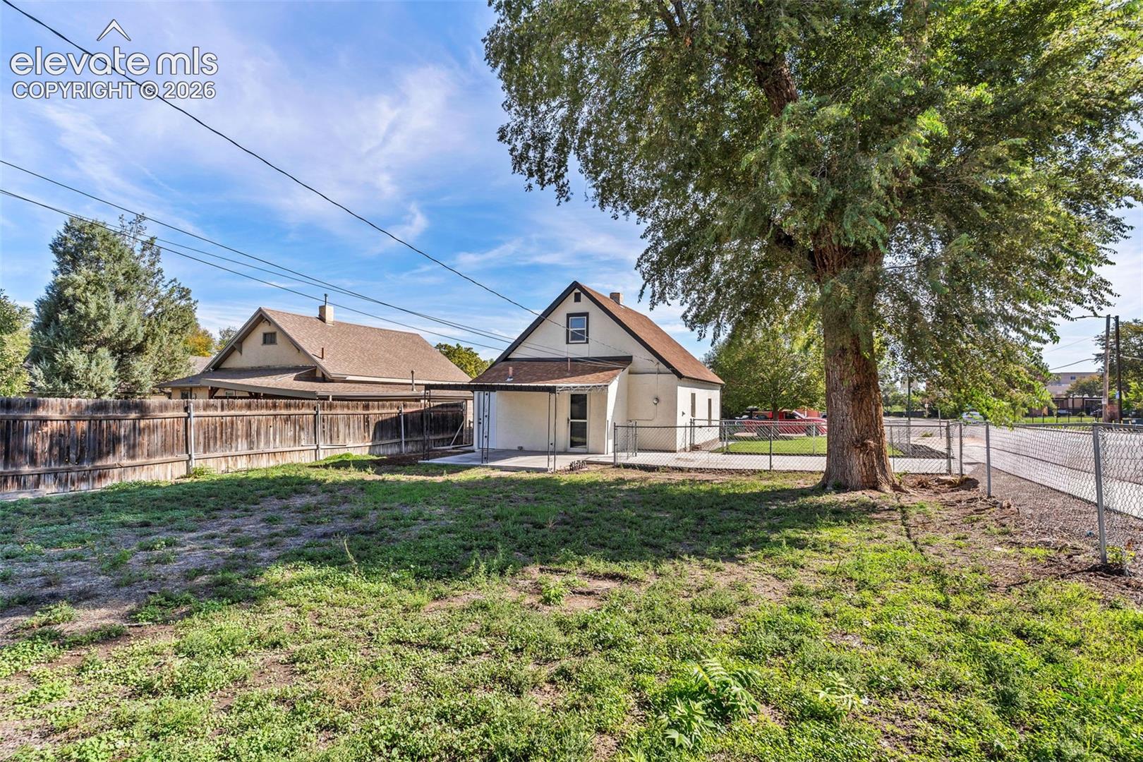Exterior lot featuring a covered rear patio, metal perimeter fencing, wood-slat privacy fencing, and a large mature tree