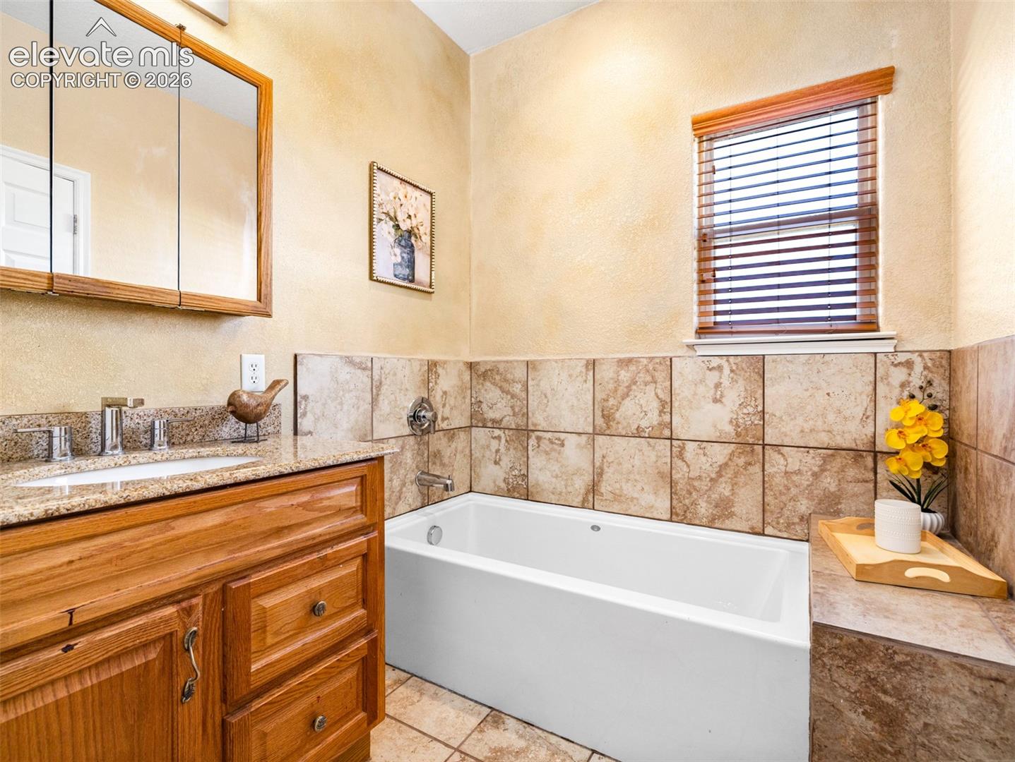 Integrated bathtub with tiled surround, wood-finish vanity with a granite countertop, and a recessed medicine cabinet