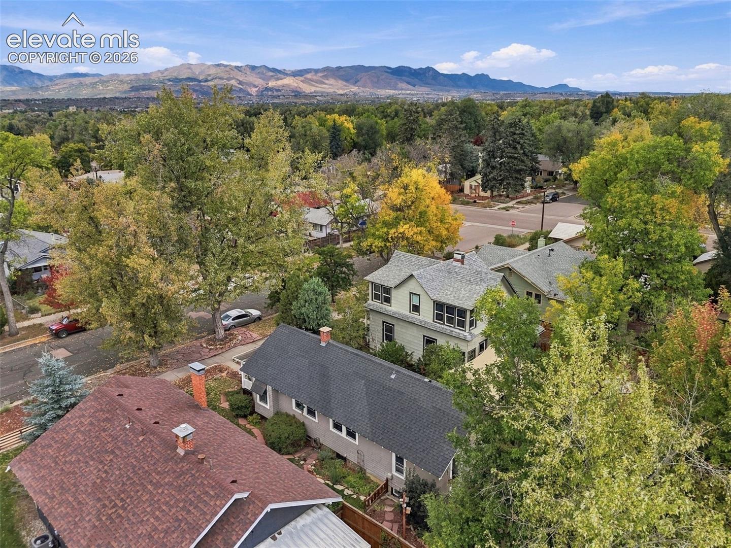 Aerial perspective featuring multi-story residential structures, mature deciduous trees, and a mountain range backdrop