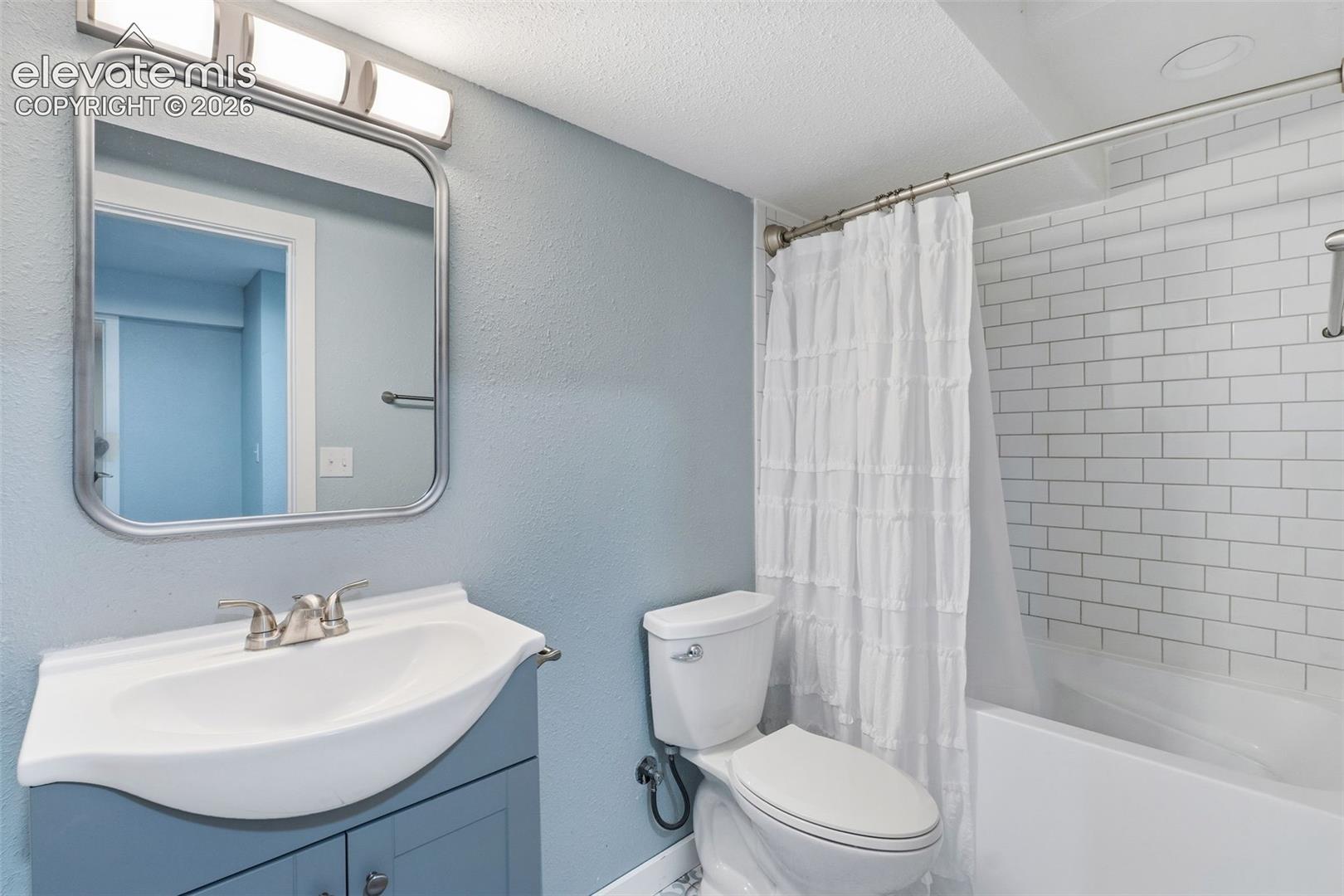 Bathroom featuring a blue vanity with an integrated sink, brushed nickel faucet, a rounded rectangular mirror, and a tiled shower-tub combination
