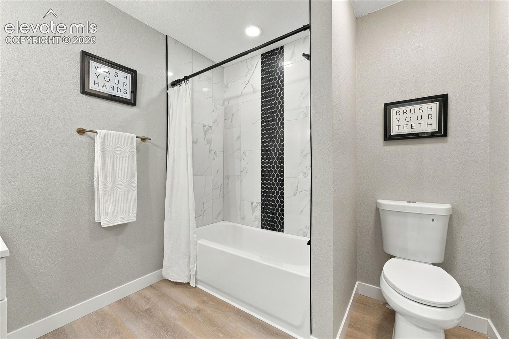 Full bathroom featuring wood-finish flooring, a built-in tub with large-format wall tile, and a decorative vertical accent strip of black hexagonal mosaic tile