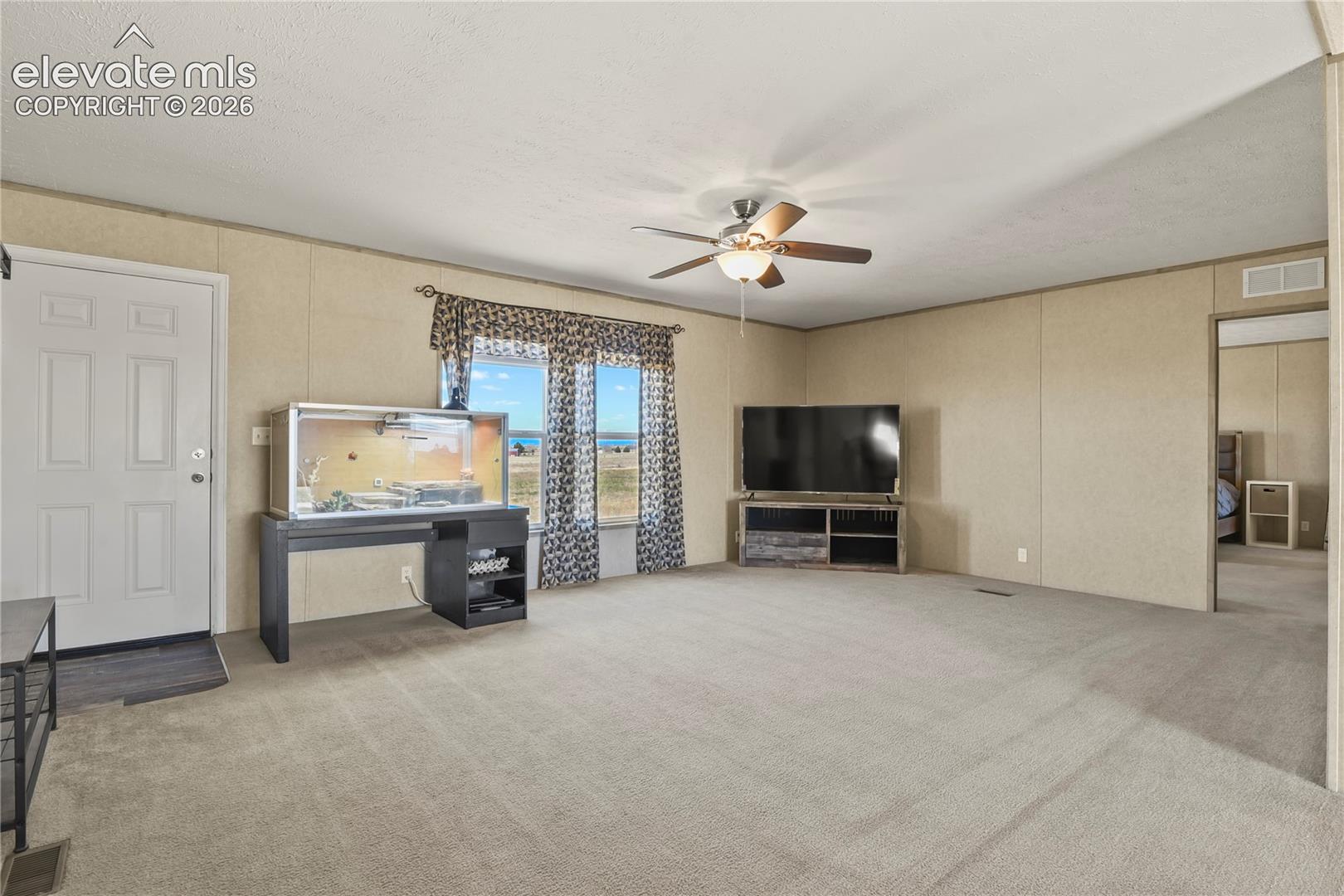 Neutral-toned carpeting, ceiling-mounted paddle fan, panel-style door, and double-pane window with exterior natural scenery