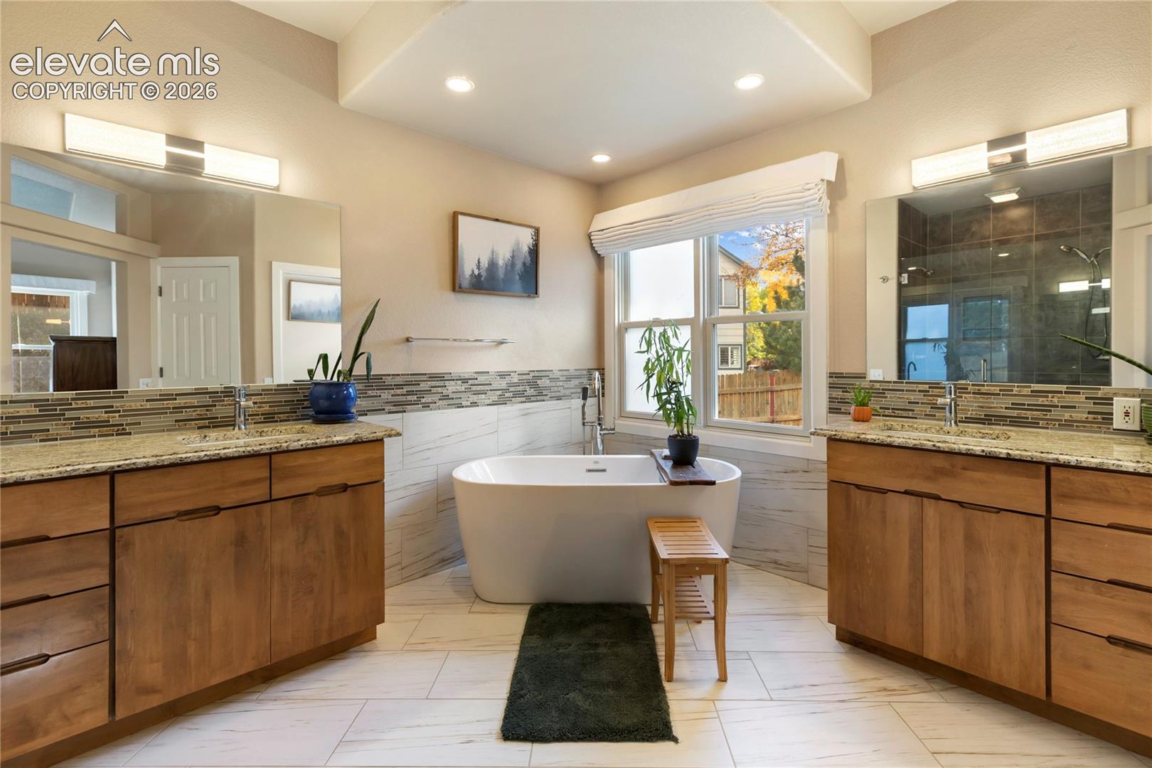 Dual wood-finish vanities with light stone countertops, integrated sinks, and individual mirrors