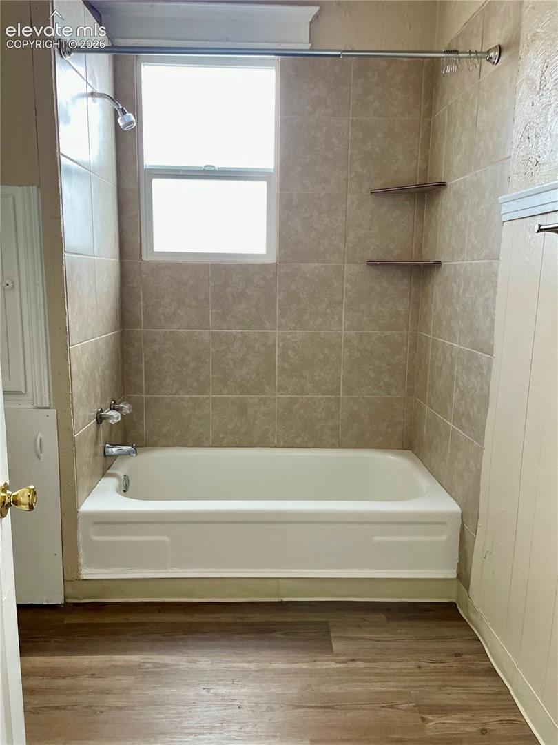 Bathtub with full tile surround, integrated window, and wood-finish flooring
