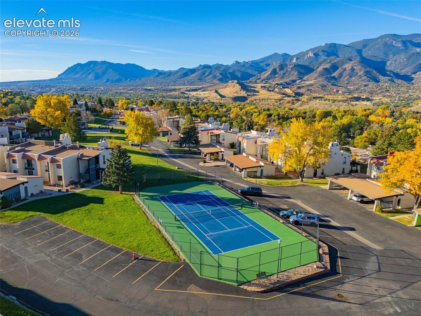 Tennis court with surrounding green fence, mountain backdrop, and stucco buildings