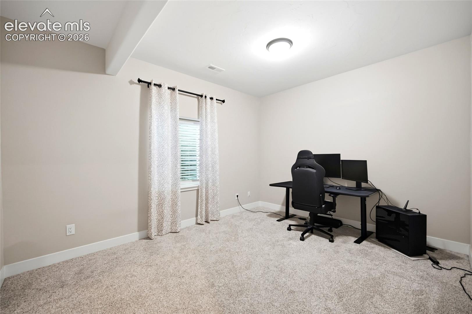 Neutral-toned interior space featuring carpeting, a single-window configuration with a curtain rod, and a ceiling-mounted light fixture