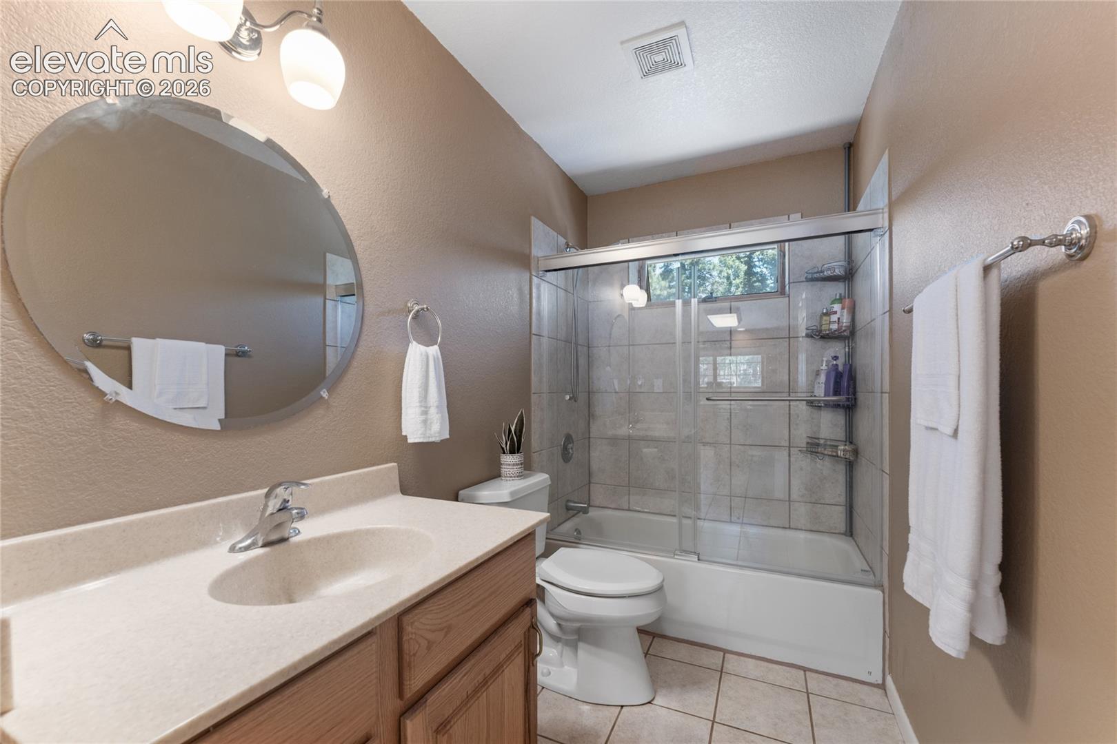 Bathroom featuring a wood-finish vanity with a built-in sink, a large oval mirror, and a shower-tub combination with sliding glass doors