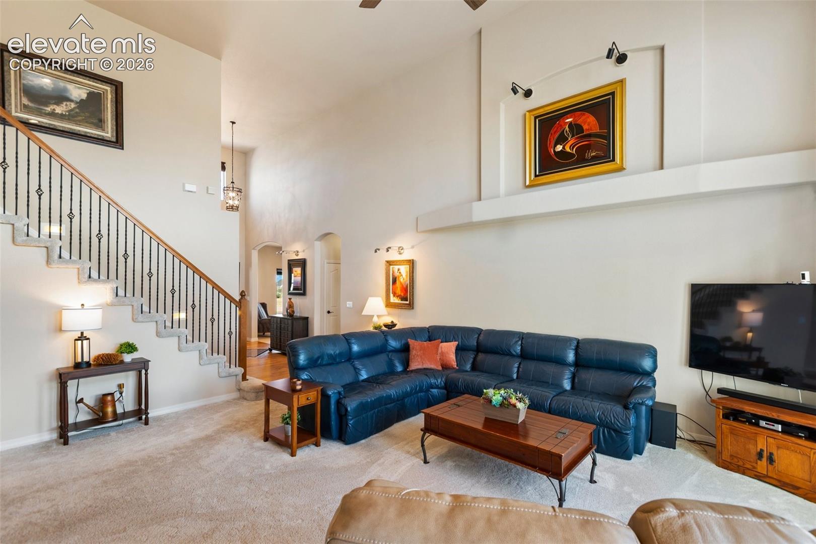 High-ceiling living area featuring a decorative wall niche, a staircase with metal balusters and wood handrail, and wall-mounted accent lighting
