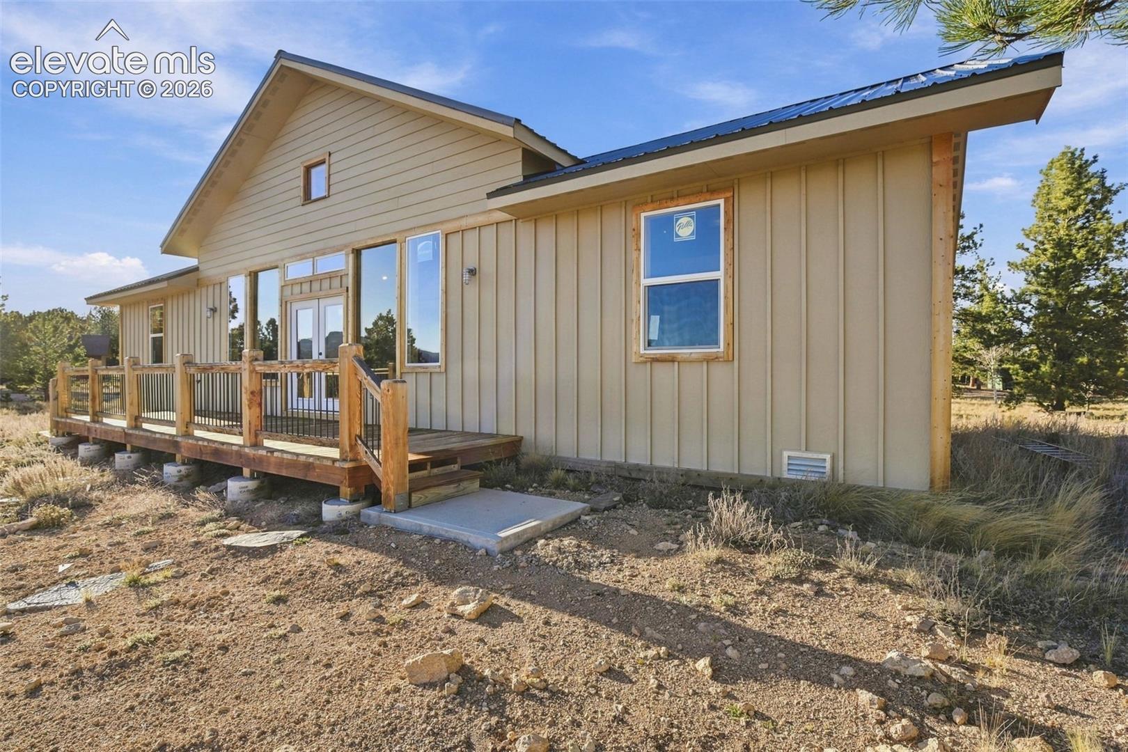 Exterior featuring board-and-batten siding, metal roofing, expansive wood deck with metal railing, and dual glass-paneled entry doors
