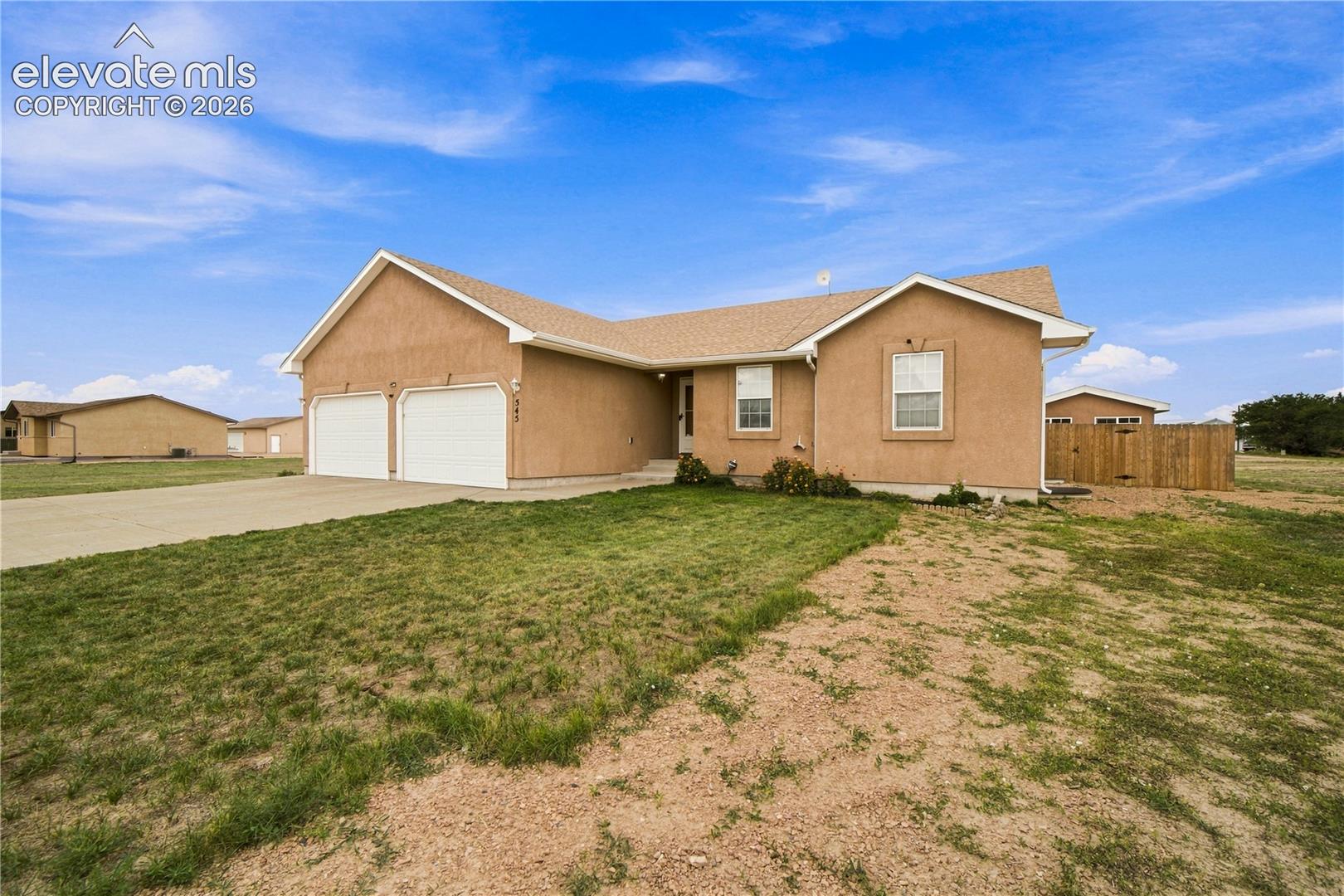 Stucco exterior with a pitched roof, attached two-car garage, concrete driveway, and partial wood fencing