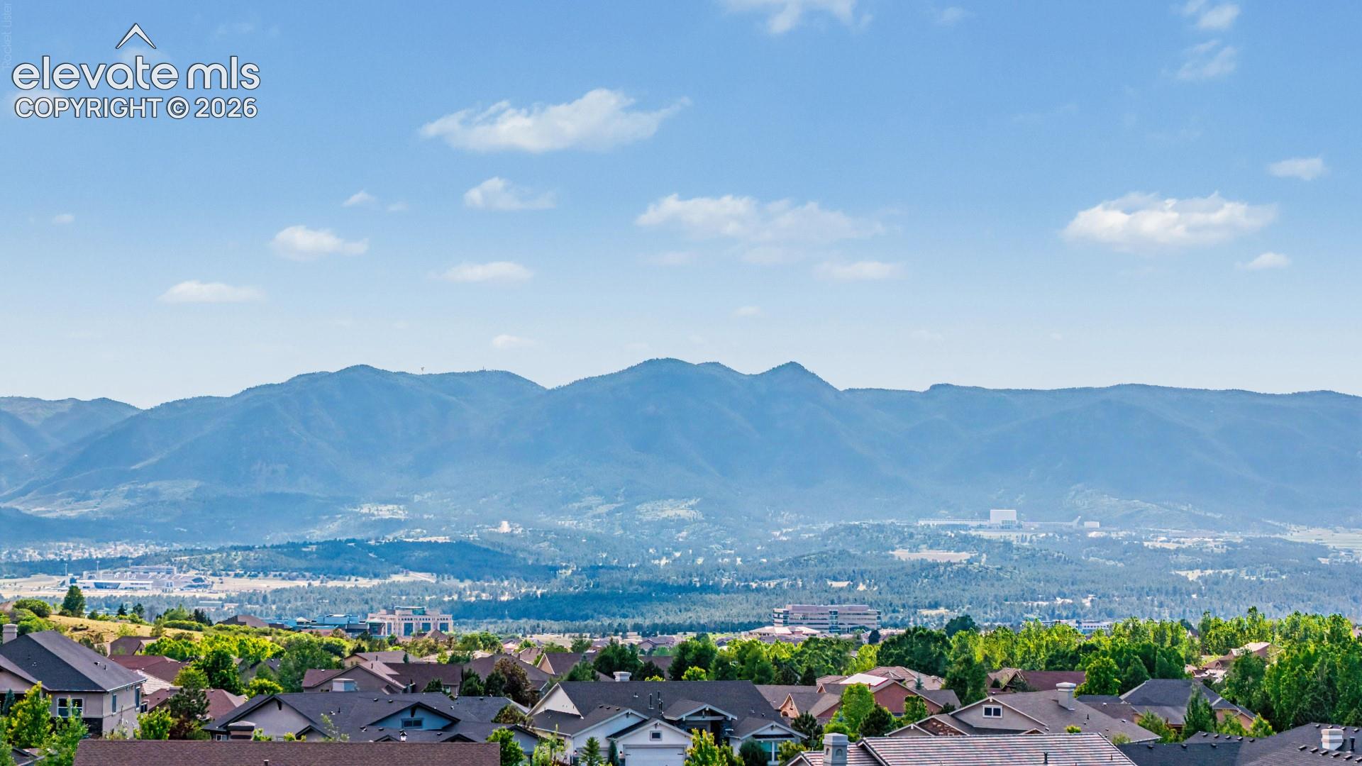 Expansive mountain range backdrop with distant city elements and a residential area with varied rooflines