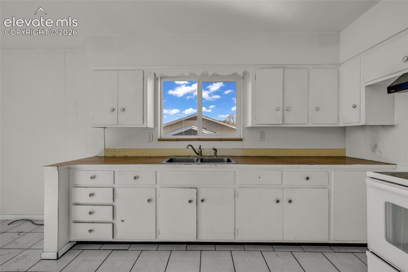 White cabinetry featuring ample storage, a stainless steel double basin sink, and a window for natural light