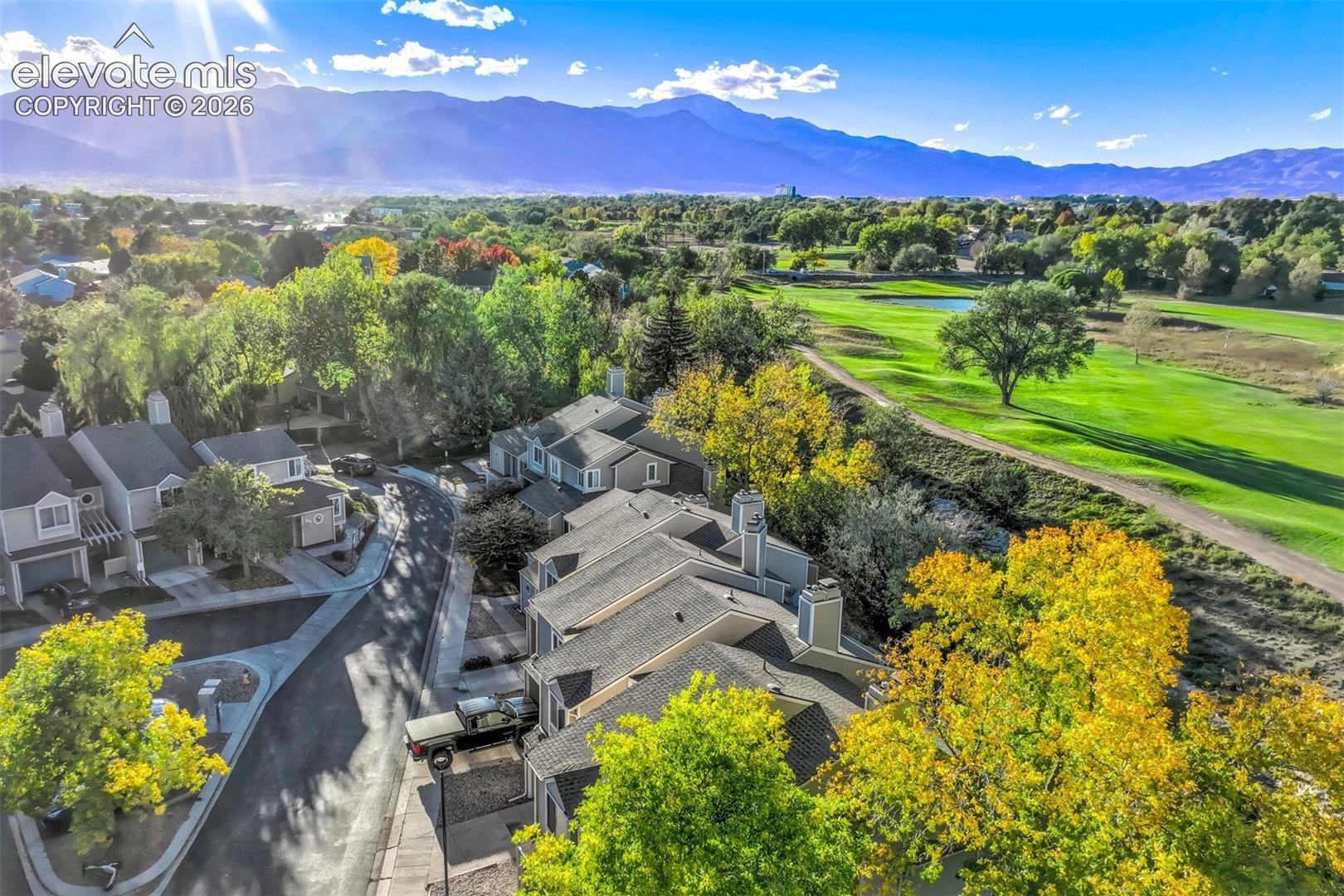 Aerial perspective featuring multi-story residential structures with asphalt shingle roofing, situated against a backdrop of mountain ranges and expansive green space