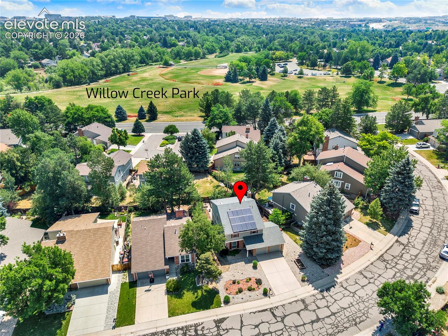 Aerial view of property featuring roof-mounted solar panels, attached two-car garage, concrete driveway, and xeriscaped front yard landscaping