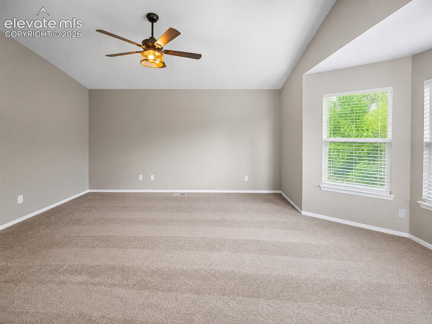 Vaulted ceiling, ceiling fan with integrated lighting, carpeted flooring, multiple windows with blinds, and neutral wall tones